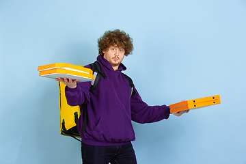 Image showing Contacless delivery service during quarantine. Man delivers food and shopping bags during insulation. Emotions of deliveryman isolated on blue background.