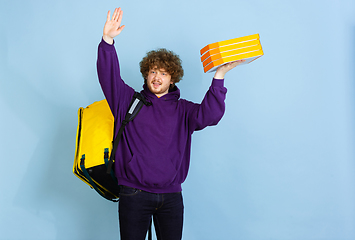 Image showing Contacless delivery service during quarantine. Man delivers food and shopping bags during insulation. Emotions of deliveryman isolated on blue background.