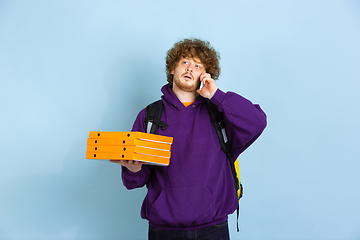 Image showing Contacless delivery service during quarantine. Man delivers food and shopping bags during insulation. Emotions of deliveryman isolated on blue background.