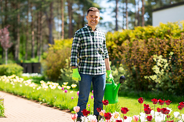 Image showing happy man with watering can and flowers at garden