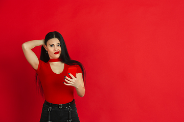 Image showing Caucasian young woman\'s monochrome portrait on red studio background, emotional and expressive