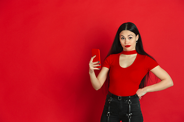 Image showing Caucasian young woman\'s monochrome portrait on red studio background, emotional and expressive