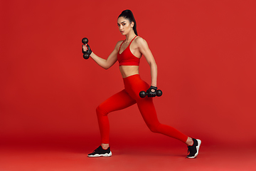 Image showing Beautiful young female athlete practicing on red studio background, monochrome portrait