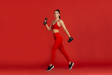 Image showing Beautiful young female athlete practicing on red studio background, monochrome portrait