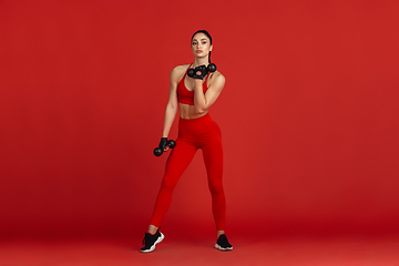 Image showing Beautiful young female athlete practicing on red studio background, monochrome portrait