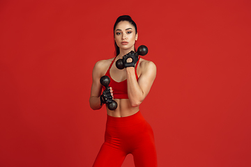 Image showing Beautiful young female athlete practicing on red studio background, monochrome portrait