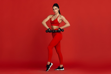 Image showing Beautiful young female athlete practicing on red studio background, monochrome portrait