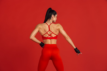 Image showing Beautiful young female athlete practicing on red studio background, monochrome portrait