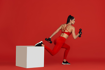 Image showing Beautiful young female athlete practicing on red studio background, monochrome portrait