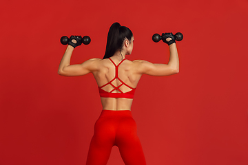 Image showing Beautiful young female athlete practicing on red studio background, monochrome portrait