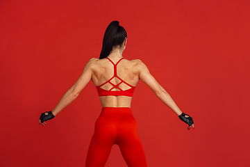 Image showing Beautiful young female athlete practicing on red studio background, monochrome portrait