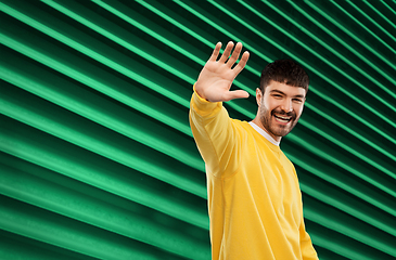 Image showing smiling young man in yellow sweatshirt waving hand