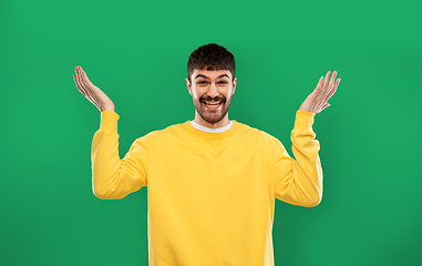 Image showing happy man in yellow sweater shrugging over green