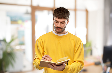 Image showing man in yellow sweatshirt writing to diary