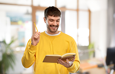 Image showing happy man in yellow sweater with diary and pencil