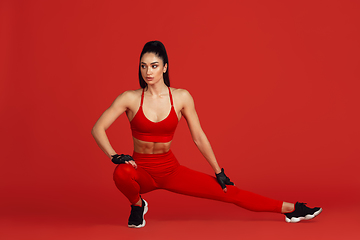 Image showing Beautiful young female athlete practicing on red studio background, monochrome portrait