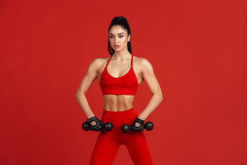 Image showing Beautiful young female athlete practicing on red studio background, monochrome portrait