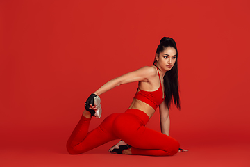 Image showing Beautiful young female athlete practicing on red studio background, monochrome portrait