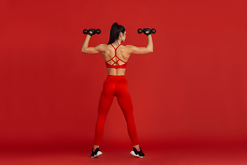 Image showing Beautiful young female athlete practicing on red studio background, monochrome portrait