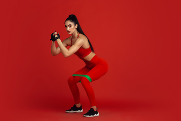 Image showing Beautiful young female athlete practicing on red studio background, monochrome portrait