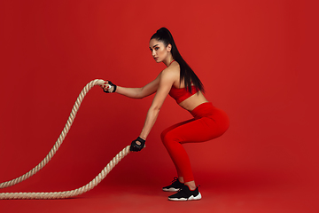 Image showing Beautiful young female athlete practicing on red studio background, monochrome portrait