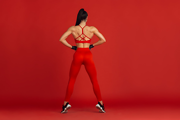 Image showing Beautiful young female athlete practicing on red studio background, monochrome portrait