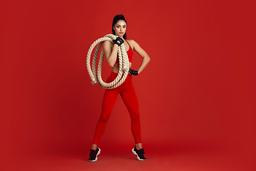 Image showing Beautiful young female athlete practicing on red studio background, monochrome portrait