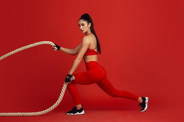 Image showing Beautiful young female athlete practicing on red studio background, monochrome portrait