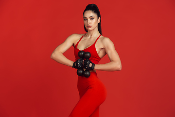 Image showing Beautiful young female athlete practicing on red studio background, monochrome portrait