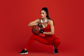 Image showing Beautiful young female athlete practicing on red studio background, monochrome portrait