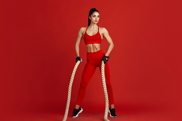 Image showing Beautiful young female athlete practicing on red studio background, monochrome portrait