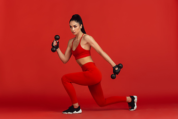 Image showing Beautiful young female athlete practicing on red studio background, monochrome portrait