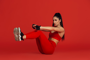 Image showing Beautiful young female athlete practicing on red studio background, monochrome portrait