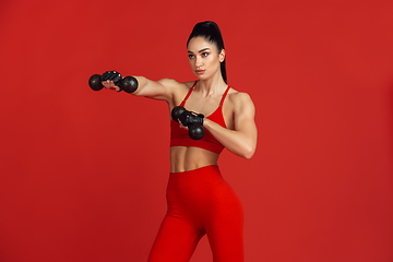 Image showing Beautiful young female athlete practicing on red studio background, monochrome portrait