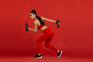 Image showing Beautiful young female athlete practicing on red studio background, monochrome portrait