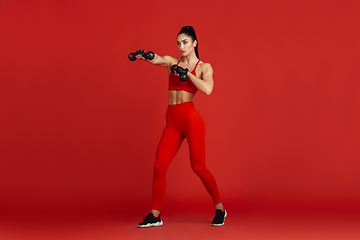 Image showing Beautiful young female athlete practicing on red studio background, monochrome portrait