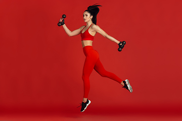 Image showing Beautiful young female athlete practicing on red studio background, monochrome portrait