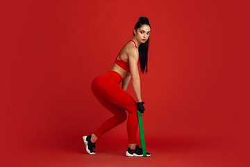 Image showing Beautiful young female athlete practicing on red studio background, monochrome portrait