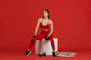 Image showing Beautiful young female athlete practicing on red studio background, monochrome portrait