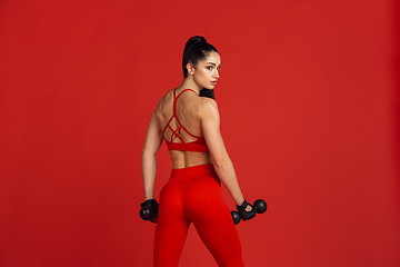 Image showing Beautiful young female athlete practicing on red studio background, monochrome portrait