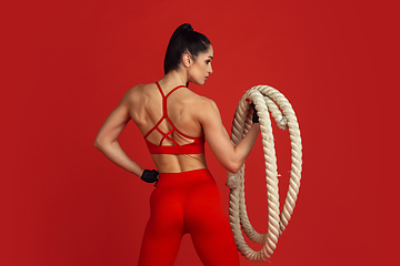 Image showing Beautiful young female athlete practicing on red studio background, monochrome portrait