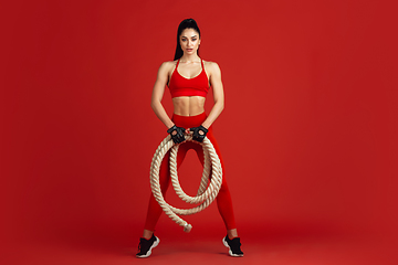 Image showing Beautiful young female athlete practicing on red studio background, monochrome portrait