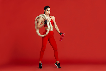 Image showing Beautiful young female athlete practicing on red studio background, monochrome portrait