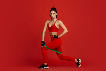 Image showing Beautiful young female athlete practicing on red studio background, monochrome portrait