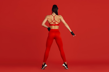 Image showing Beautiful young female athlete practicing on red studio background, monochrome portrait