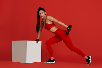 Image showing Beautiful young female athlete practicing on red studio background, monochrome portrait