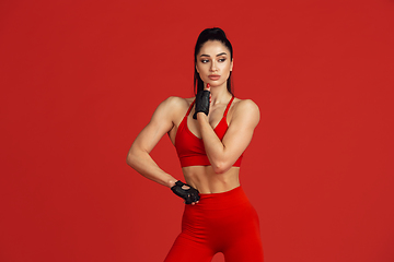 Image showing Beautiful young female athlete practicing on red studio background, monochrome portrait