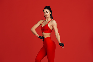 Image showing Beautiful young female athlete practicing on red studio background, monochrome portrait