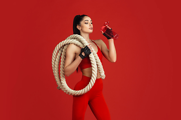 Image showing Beautiful young female athlete practicing on red studio background, monochrome portrait