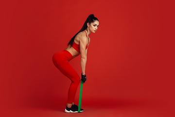 Image showing Beautiful young female athlete practicing on red studio background, monochrome portrait